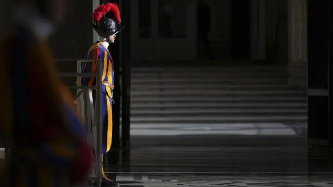Soldado da Guarda Suíça parado, no Vaticano. Ele usa as vestes tradicionais, azul, amarela e vermelha.