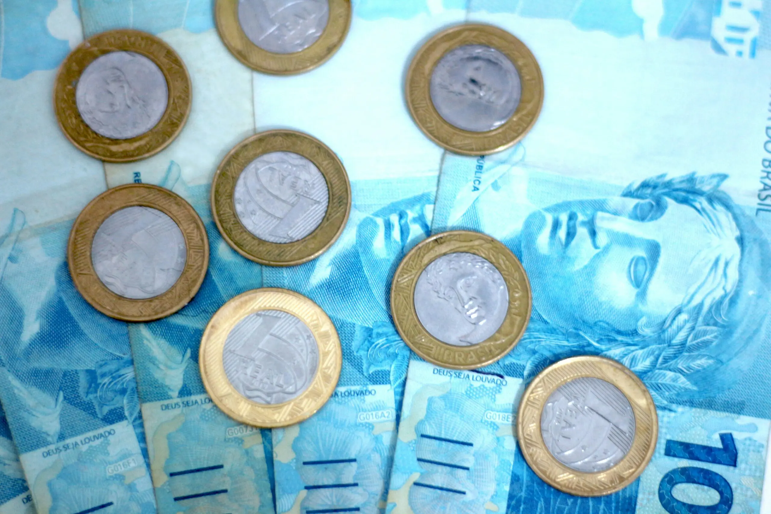 Moedas de um real junto com notas de cem reais.