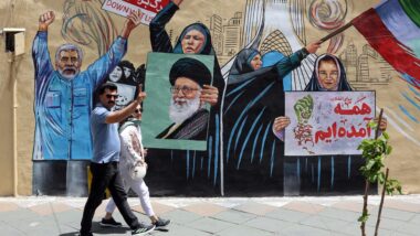 Casal iraniano caminha em frente a mural que critica ataques de Estados Unidos e Israel em Teerã, capital do país